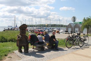 A waterfront scene with a statue, people sitting on benches, and boats in the background. - 2) Holiday apartment 3-room, upper floor, 90m² - Landhaus Alte Schule near (Alt Bukow)