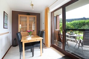 Un coin repas avec une table et des chaises en bois, un buffet avec des portes en verre et une vue sur un patio aménagé avec du mobilier d’extérieur.