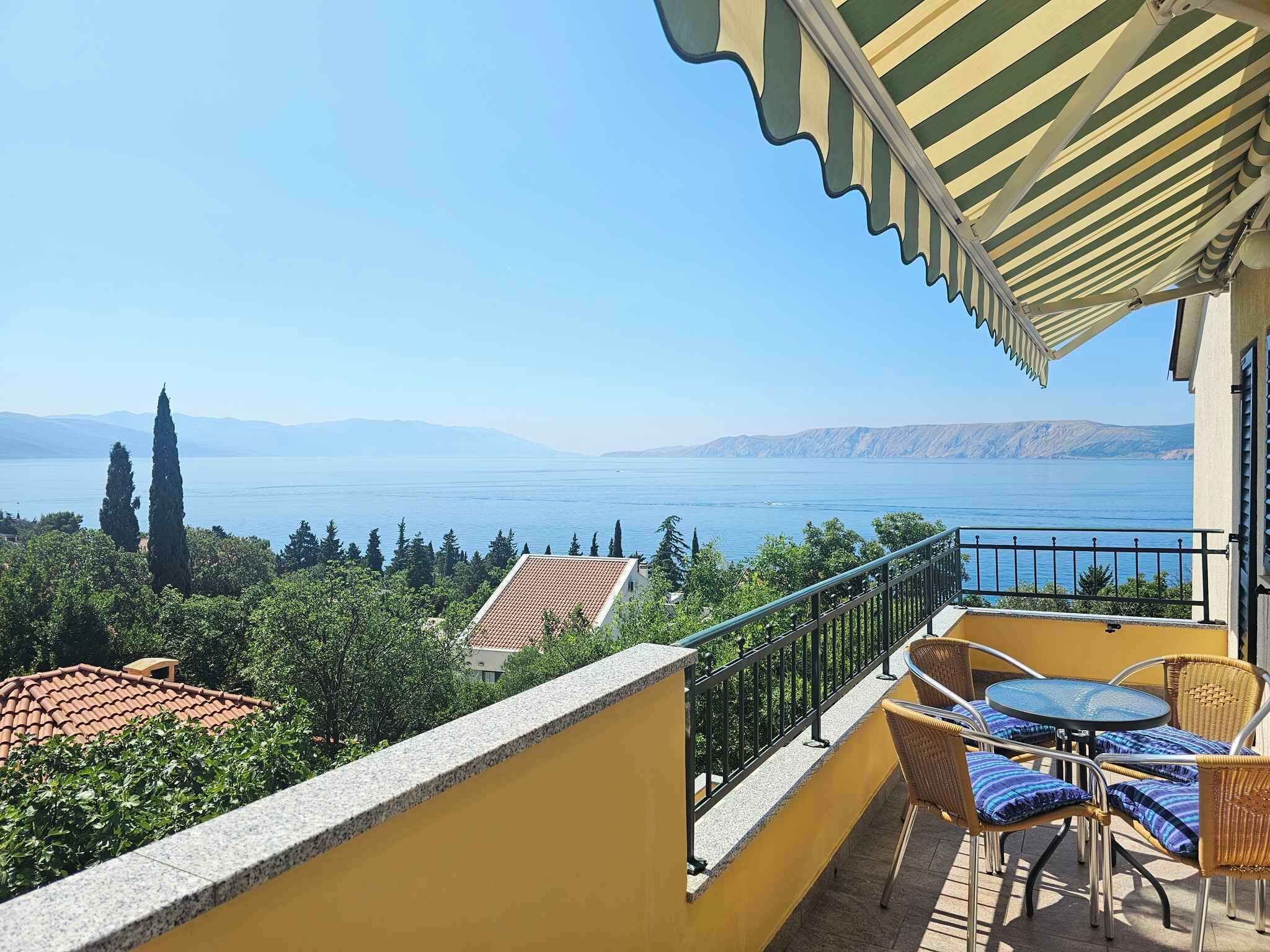 A balcony with a view of a lake and mountains, wicker furniture, and a yellow wall.