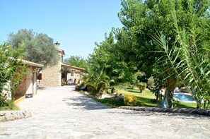A stone pathway leading to a stone building with a chimney, surrounded by greenery and a pool.