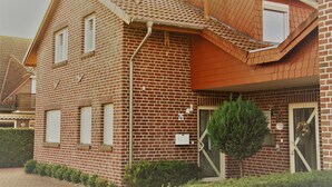 Uma casa de dois andares de tijolo com telhado inclinado, uma árvore pequena na frente e uma caixa de correio na parede.