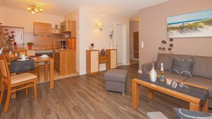Un apartamento moderno con cocina, comedor y sala de estar. Incluye muebles de madera, un sofá, una mesa de centro y un cuadro con una escena de playa.