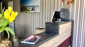 Una mesa de recepción con un cuadro enmarco de una escena de playa, un jarrón con flores secas y un libro titulado "EN JAHRE MIT EISEN".