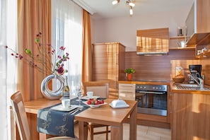 A modern kitchen with wooden cabinets, a built-in oven, and a dining area with a table set for two. - Type II / Nr. 1 - Strandhaus Aurell - directly on the Baltic Sea beach (Heringsdorf)