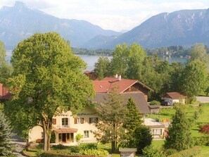 Un albergo con un grande albero di fronte, montagne sullo sfondo e vista sul lago.