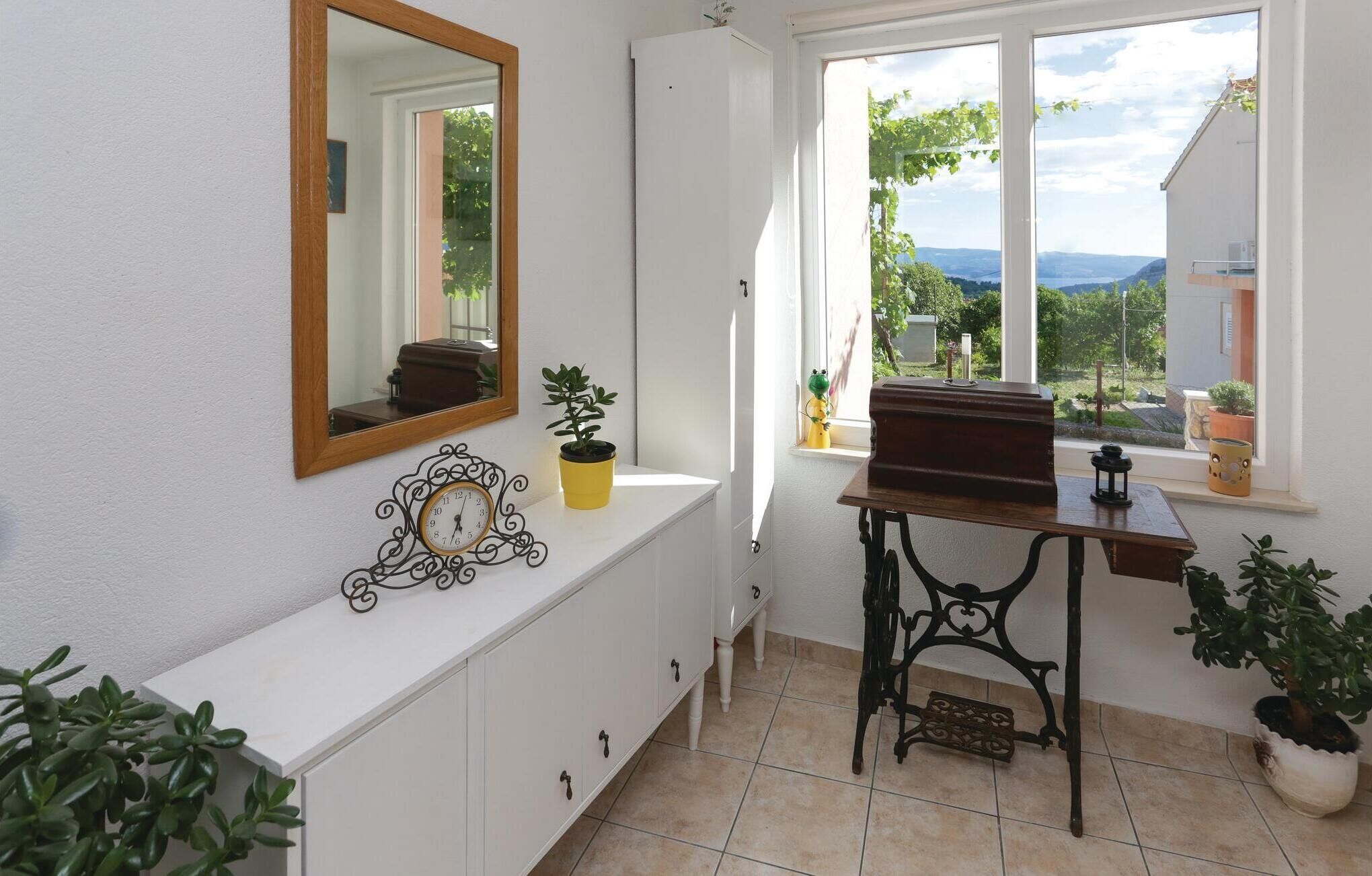 A bathroom with a white vanity, a mirror, a clock, and a window with a view of the outdoors.