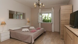A bedroom with a bed, bedside lamps, a TV, a window with curtains, and a mirror on the wall.