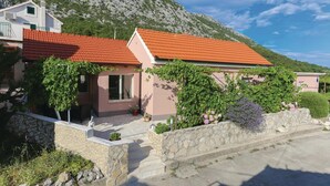 A two-story building with a red-tiled roof, stone walls, and a garden with various plants and flowers.