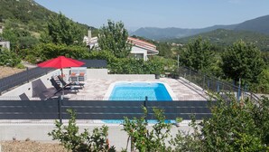 A swimming pool with a view of mountains, a red umbrella, and lounge chairs.