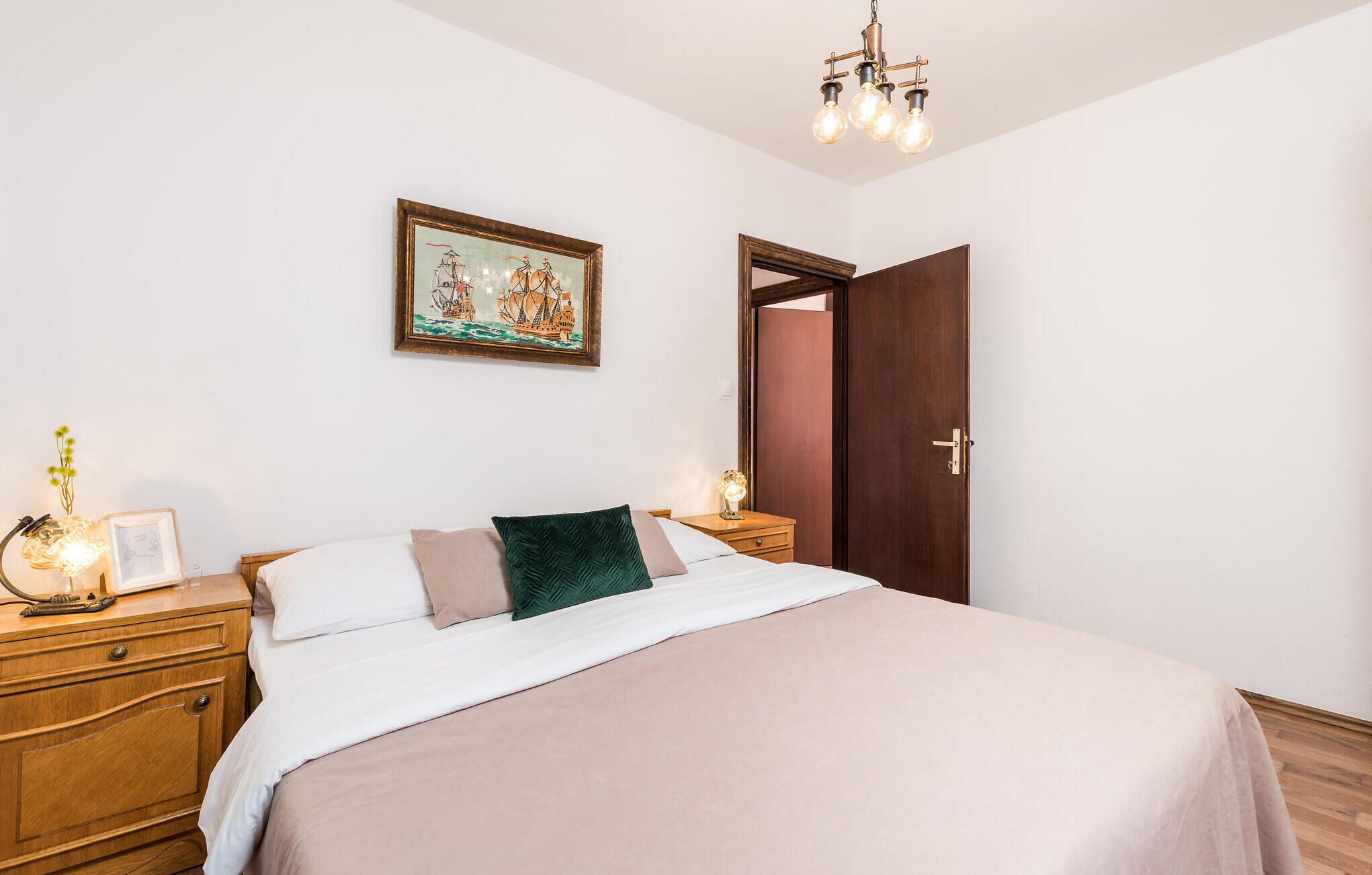 Una camera da letto con un letto, un comodino, una lampada da comodino, un quadro incorniciato, una porta e un lampadario.