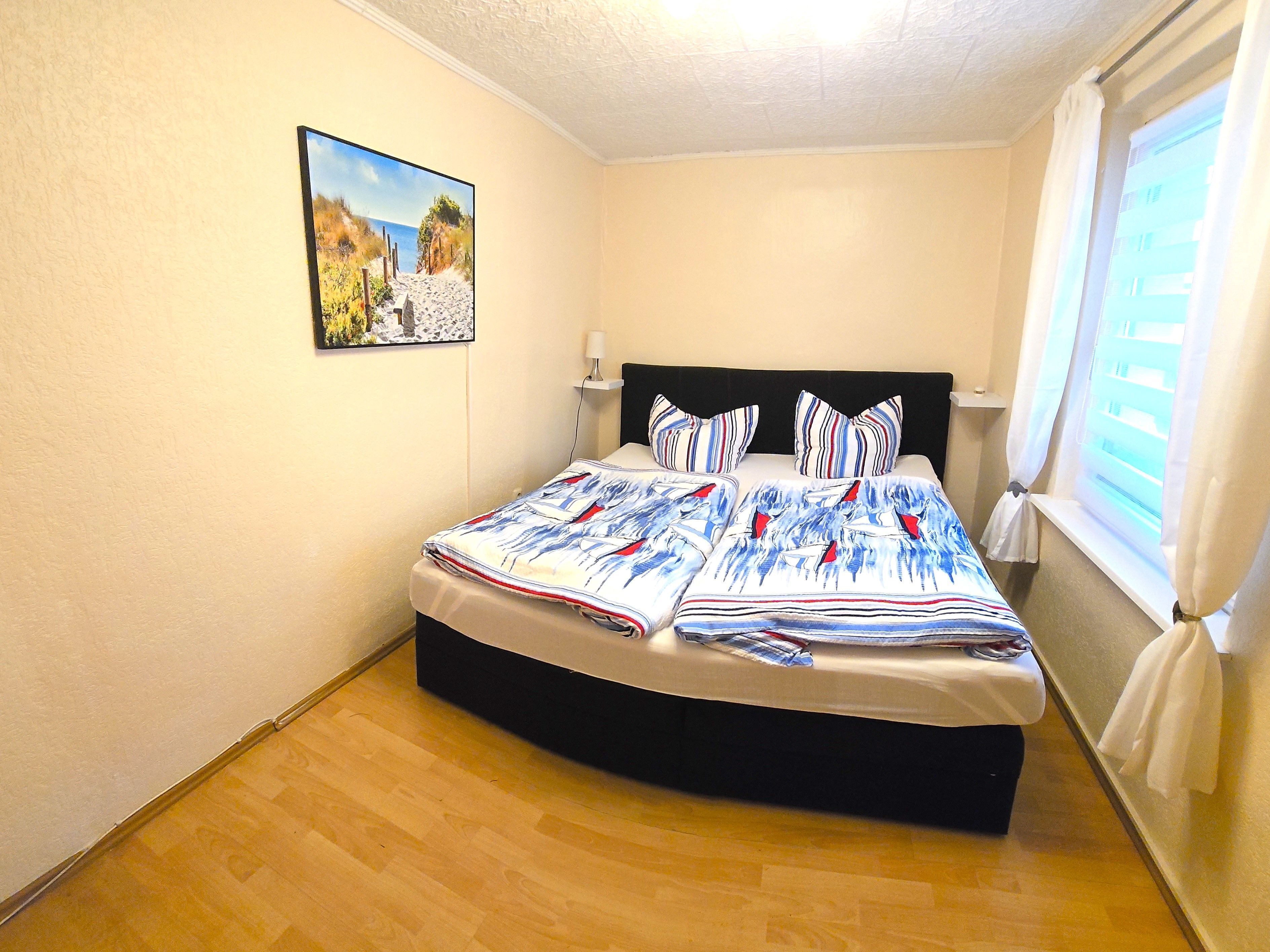 Een slaapkamer met een bed, een schilderij aan de muur en een raam met gordijnen.