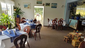 Un espace repas avec plusieurs tables et chaises, dont certaines sont recouvertes de nappes bleues. On y trouve également des plantes en pot et des œuvres d’art accrochées aux murs.