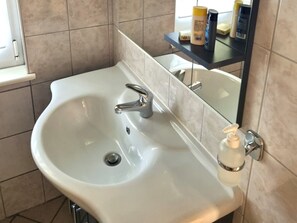 A bathroom with a white sink, a mirror, and toiletries on a shelf.