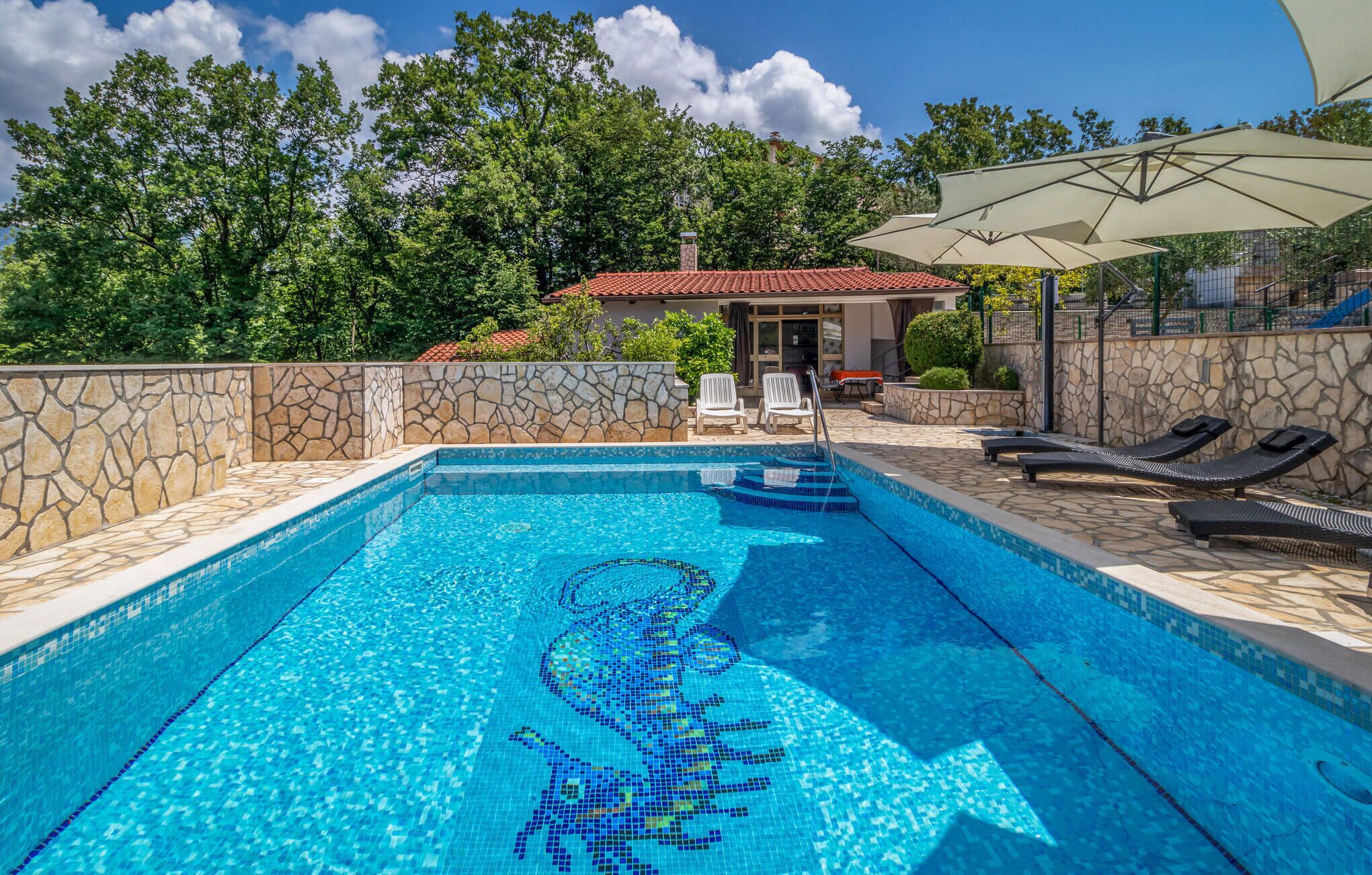 A swimming pool with mosaic tiles, stone walls, and lounge chairs.