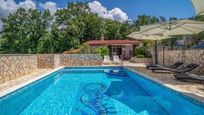 A swimming pool with mosaic tiles, stone walls, and lounge chairs.