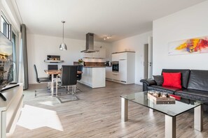 A modern living room with a glass coffee table, a black leather sofa, and a dining area with a wooden table and chairs. - Apartment Saphir with penthouse flair - Oasis on the lagoon - Saphir (2-10a) (Garz/Usedom)