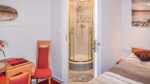Ein Hotelzimmer mit Dusche, einem Bett, einem Sessel, einem Tisch und einem Wandbild.