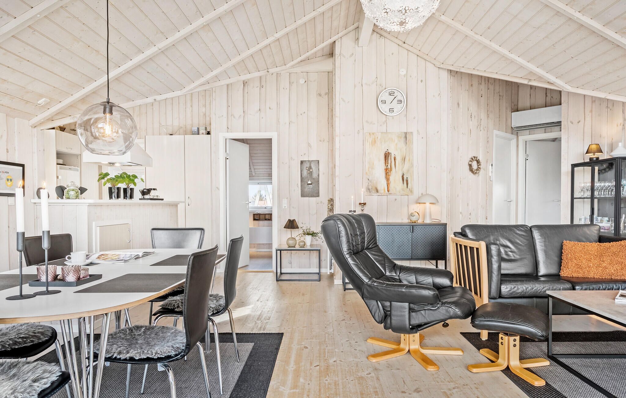 A spacious living area with a high ceiling, a dining table with chairs, a black leather sofa, and a blue sofa.