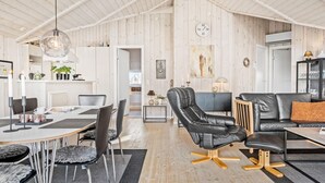 Een ruime woonkamer met een hoge plafond, een eettafel met stoelen, een zwarte leren bank en een blauwe bank.