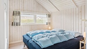 Een slaapkamer met een bed, een raam met gordijnen en houten wanden.