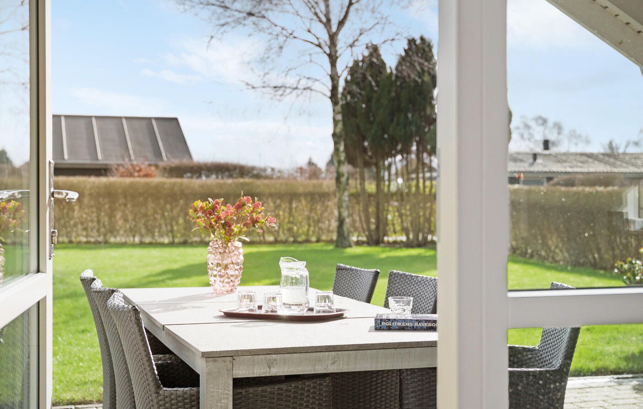 Een terras met een tafel voor vier personen, omringd door rieten stoelen. Op de tafel staat een vaas met bloemen en een dienblad met glazen.
