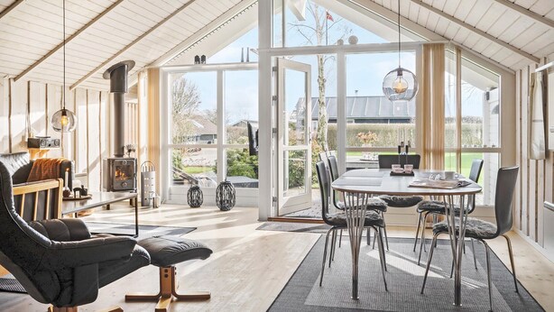 Een ruime kamer met een groot raam, een eettafel met stoelen, een bank en een open haard.