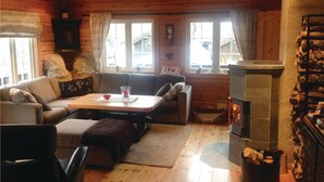 Een gezellig chaletinterieur met een bank, een tafeltje, een open haard en een raam met gordijnen.