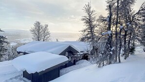 Een blokhut omringd door met sneeuw bedekte bomen en een besneeerd landschap.
