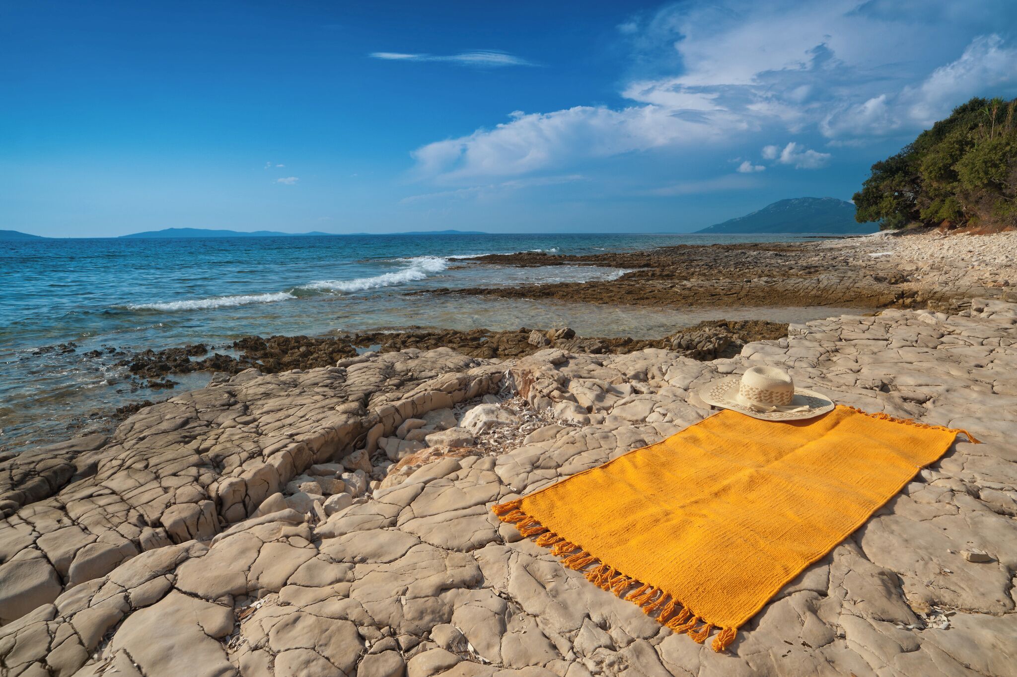 Una spiaggia rocciosa con una coperta gialla e un cappello.