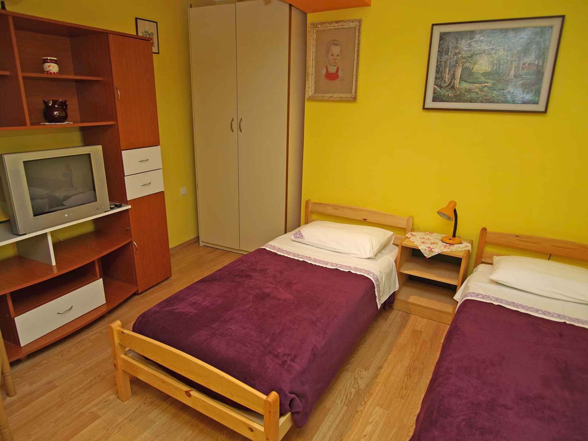 A room with two beds, a wardrobe, a television, and a painting on the wall.