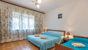 A bedroom with two beds, wooden flooring, floral curtains, a ceiling light, and a small painting on the wall. - 2 bedroom awesome apartment in Fazana (Fazana)