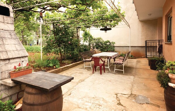 A patio with a stone table and chairs, surrounded by potted plants and a pergola with climbing plants.