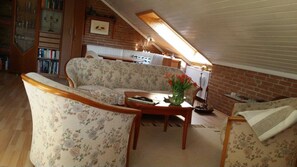 A cozy attic room with a wooden ceiling, a sofa, a coffee table, and a bookshelf. - Fewo Groß - Holiday home Asel (Vöhl)
