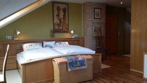 Une chambre avec un grand lit, un banc en bois, un mur en briques et une porte.