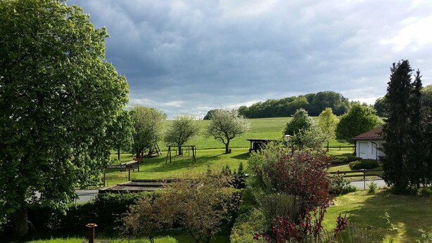 Un paysage rural avec un champ d’herbe, des arbres et un petit bâtiment.