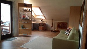 Une pièce chaleureuse avec un bureau en bois, un canapé vert et une bibliothèque remplie de livres et d’objets décoratifs.