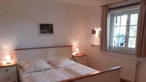 Un dormitorio con cama, mesitas de noche, una ventana con cortinas y una lámpara fijada a la pared.
