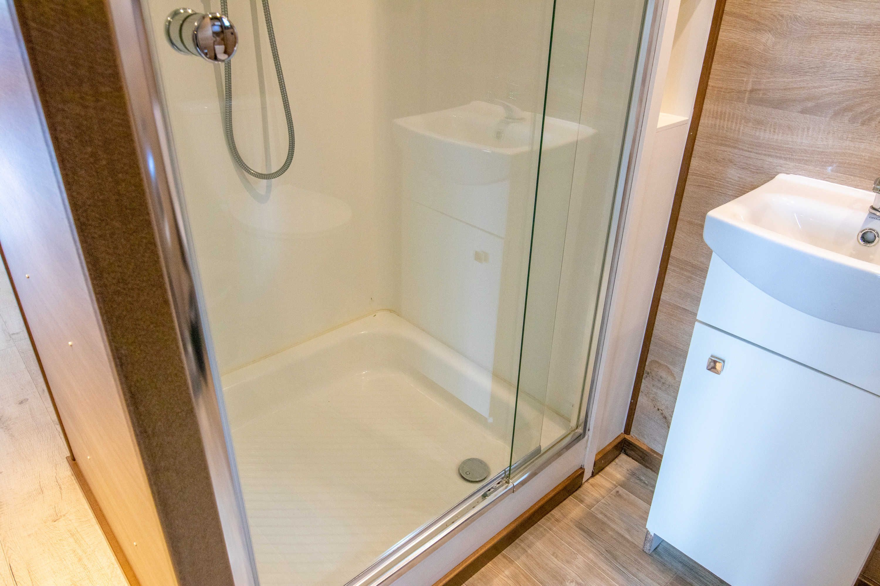 Eine Duschkabine mit Glas, ein weißes Waschbecken und eine Toilette.