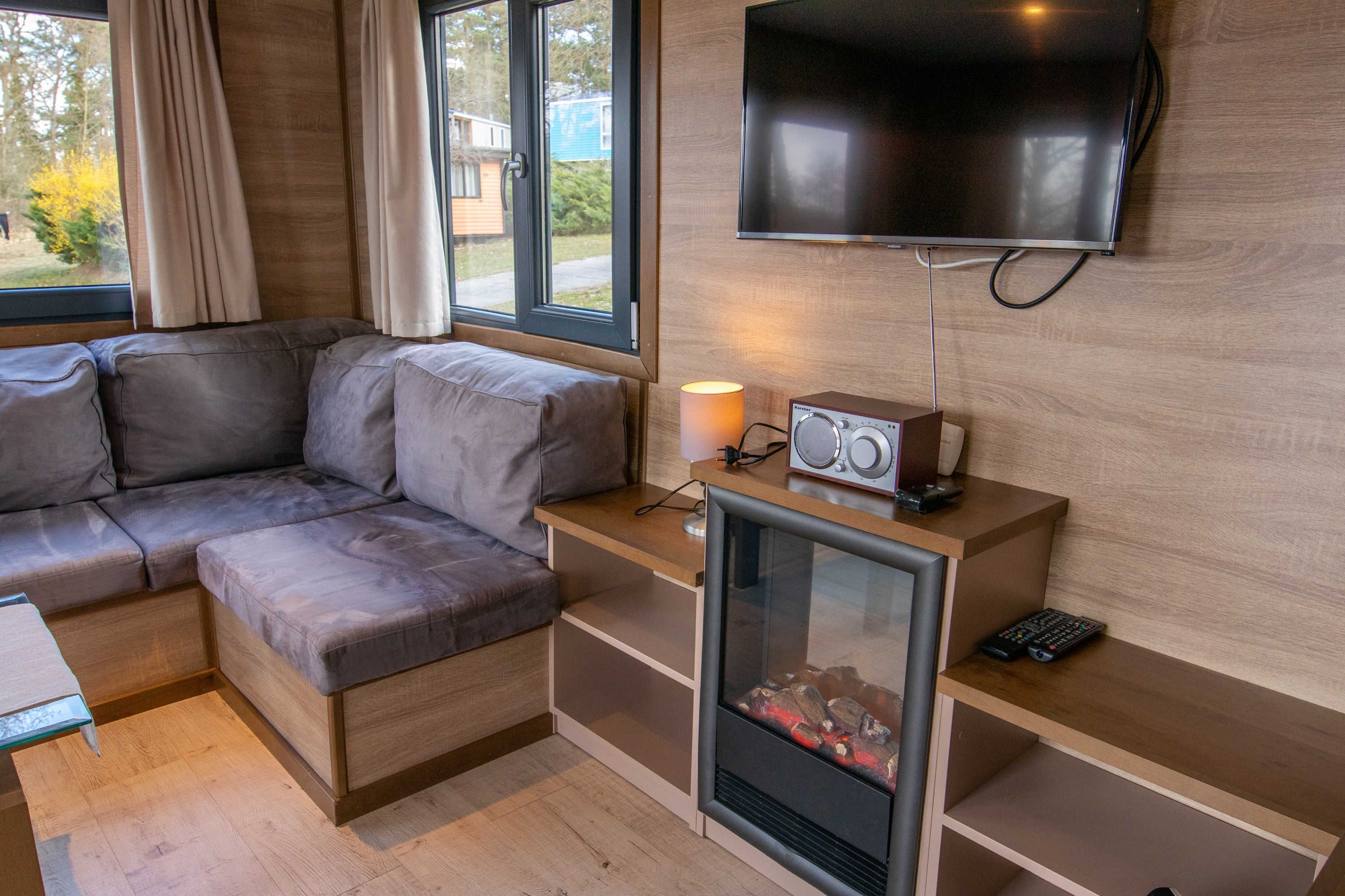 Una sala de estar moderna con un sofá seccional, una chimenea, un televisor montado en la pared y una mesita con una lámpara.