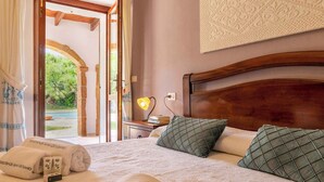 A hotel room with a bed, two pillows, a bedside lamp, a nightstand, and a view of a pool and greenery through an open door. - Holiday home with air conditioning (Alghero)