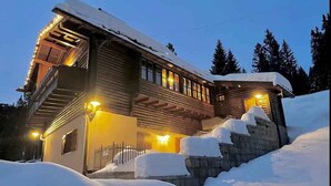 En timmerstuga med ett snötäckt tak och en mur av sten som fungerar som stödmur.