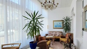 Une pièce meublée de meubles en osier, avec deux plantes en pot, un lustre et un tableau accroché au mur.