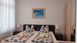Un lit double avec une literie à motifs, deux tables de chevet avec des lampes, un tableau encadré au mur et une fenêtre avec des rideaux légers.