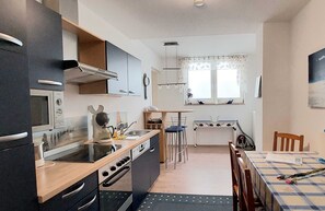 A compact kitchen with a microwave, stove, and sink. There is a dining area with a table and chairs.