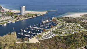 Une vue aérienne d’une marina où sont amarrés de nombreux bateaux, d’un grand bâtiment doté d’un toit végétalisé et d’un quartier résidentiel avec des maisons.