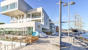 Un hôtel moderne doté d’une terrasse sur le toit, d’un espace extérieur aménagé et offrant une vue sur le port de plaisance.