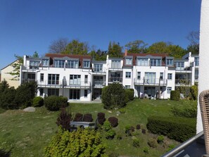 A modern multi-story residential building with balconies, a well-maintained lawn, and surrounding greenery.
