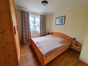 A room with a wooden bed, a window with curtains, a radiator, and a framed picture on the wall.
