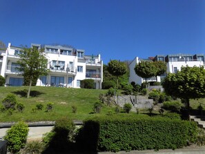 A residential building with multiple balconies, a grassy slope, and a staircase leading up to the entrance.
