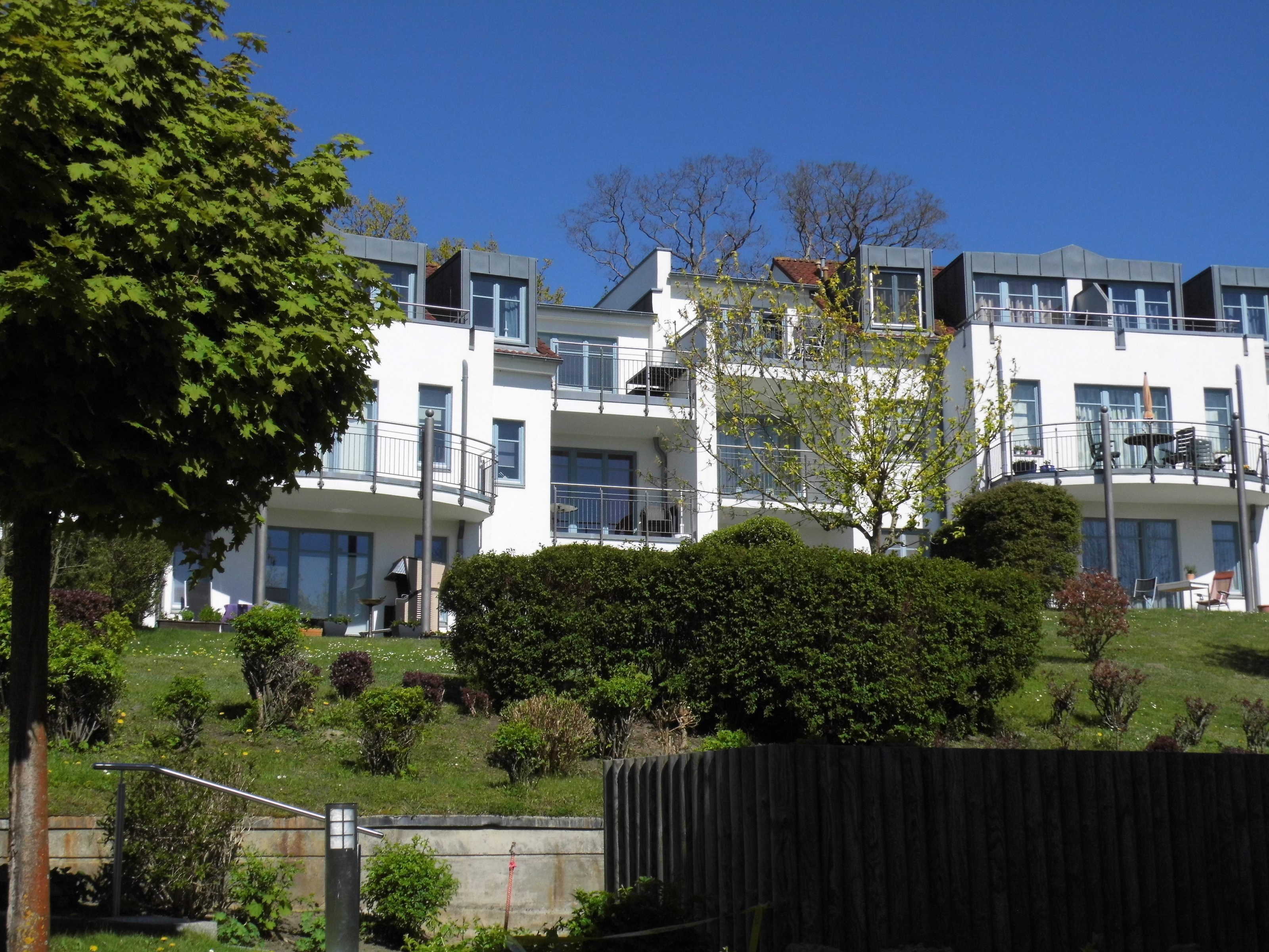 A multi-story building with balconies, surrounded by greenery and a fenced area.